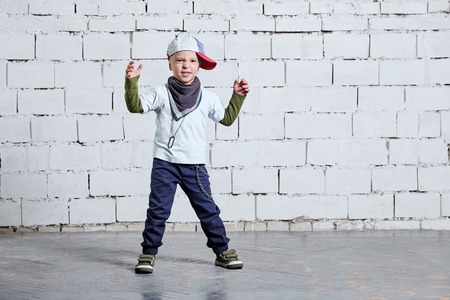 Cool kid boy dancing break dance.Hip-hop style. studio, brick wall background. Little rapper chiild man wears a cap, sneakers, pants, t-shirt, street style clothes.の写真素材