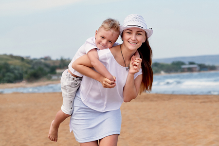 Young mother walks on beach with son. Portrait girl and child boy hugging, smiling. lifestyle, summer day. Ð¡arefree playing on outdoor sand,sea, joy, fun. concept of holiday, vacation.の写真素材
