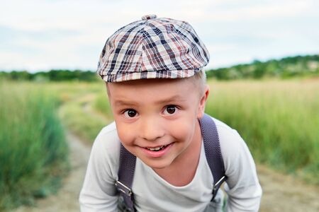 Funny happy child close-up. Attractive little boy looks into the camera with interest. Little kid smiling wears stylish cap, summer day. Pleased portrait.の写真素材
