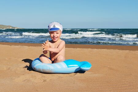 Happy baby sitting on the beach at leisure playing. little boy smiles while resting on a vacation, on a warm summer sunny day. Resort, lifestyle.の写真素材