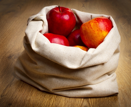 Red ripe apples in burlap sack on wooden tableの写真素材