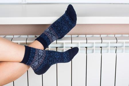 Woman's legs in socks on white radiator backgroundの写真素材