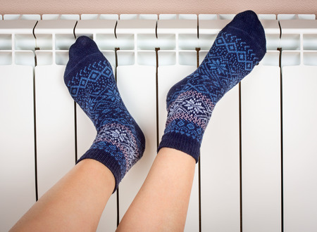 Woman's legs in socks on white radiator background