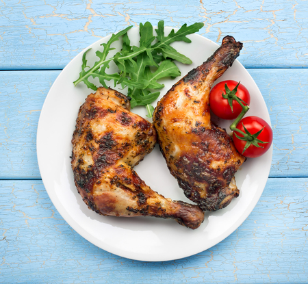 Roasted chicken legs with cherry tomatoes on blue wooden table backgroundの写真素材
