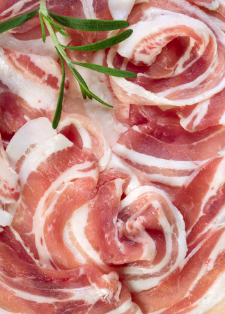 Sliced raw fresh pork bacon with leaf of rosemary, food backgroundの写真素材