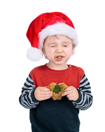 Little boy with Santa hat eating Christmas gingerbread isolated on white backgroundの写真素材