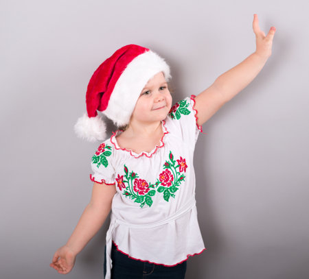 Pretty baby girl in santa claus christmas red hat on gray background, studio shotの写真素材