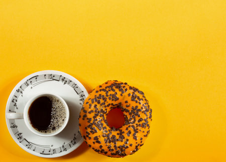 Top view of coffee cup and sweet donut with chocolate on yellow backgroundの写真素材