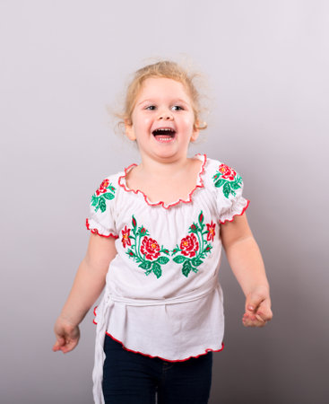 A sweet little round-faced girl in a smart embroided shirt on gray background. studio shotの写真素材