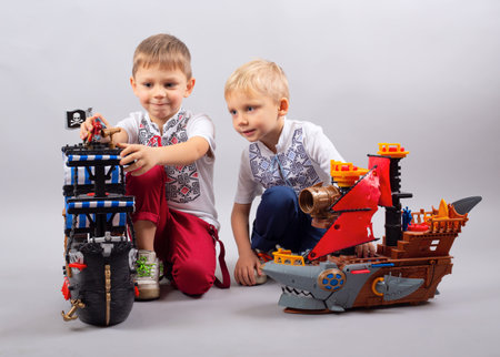 Two little kids boys playing with sailing ship model indoors. Excited children, siblings and best friends with yacht having fun, studio shot. Happy twins building and creating toys.の写真素材