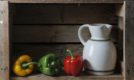 bodegon in a wooden box with a pitcher and three peppersの写真素材