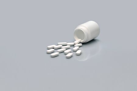 Side view of a bottle and scattered white pills on a gray background. Space for text. vitamins....