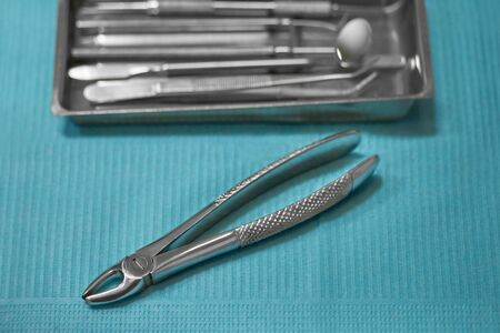 dental forceps for wisdom tooth extraction, dental extraction forceps, on a blue background, in the background a tray with dental instrumentsの写真素材