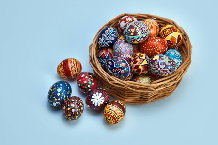 Still life with an Easter egg decorated with Easter eggs stand in a wicker basket on a blue...