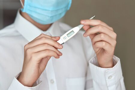 Close-up shot, a man looks at a thermometer. a man in a medical mask measures the temperature....