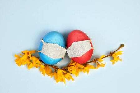 Easter eggs in a protective medicine mask on a blue background, yellow flowers. Easter quarantined...