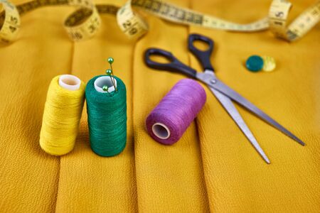 spool with green, yellow, violet thread and pins, scissors, centimeter tape for sewing on yellow...
