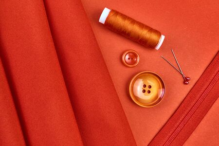 spool of red thread, buttons, pins, lock on red fabric. sewing skills, sewing supplies.の写真素材