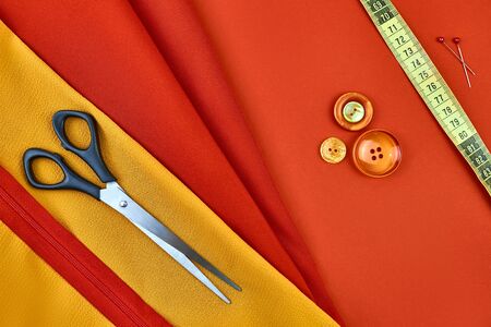 on red fabric are sewing supplies, sewing tape, scissors, buttons, pins, a sewing lock. sewing...