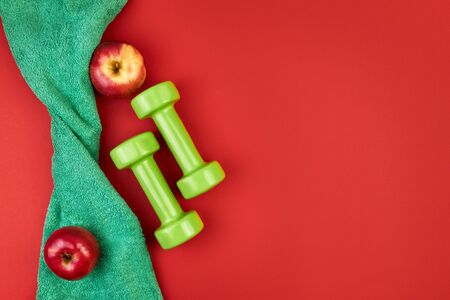 sport, green dumbbells, towel and red apple on a red background. Mockup for women workout plan for the summer season. Healthy lifestyle and nutrition, body slimming concept. It takes care of the body. Empty space for text.の写真素材