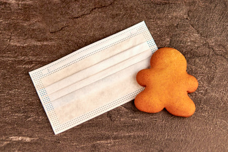 festive gingerbread near a surgical protective mask on a dark background. Christmas during the ...