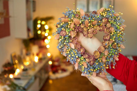 Christmas decoration of dried flowers in the form of a heart holding female hands on a Christmas background, 2021の写真素材