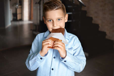 white boy 8-10 years old bites chocolate, on a dark background. sweet lover.の写真素材