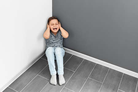 a boy of 7-10 years old sits in a corner on the floor and cries a lot. punishing children. Bad learning.の写真素材