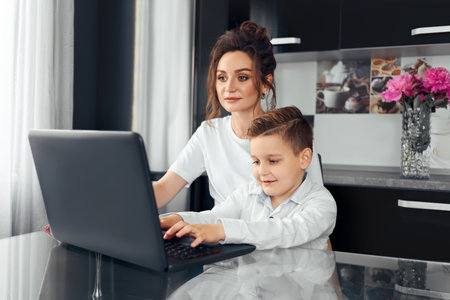distance learning, online learning at home during the covid-19 pandemic. Family, mom and son happily doing homework in the room using a laptop.の写真素材