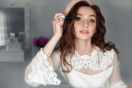 Young sexy woman looks in the mirror and applies makeup, paints eyelashes with black mascara.