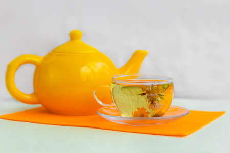 Tea. glass mug of flower tea with yellow beauty flower inside, on the table with yellow napkin and yellow teapot - tea timeの写真素材