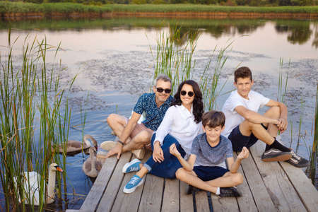 Happy family sitting on a pier on a lake or pond, relaxing in nature