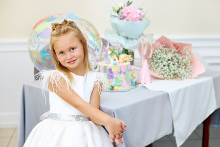 A five-year-old blonde girl birthday girl with a cake is waiting for guests. holiday. birthday is five years old.の写真素材