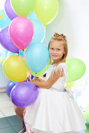 A beautiful blonde girl five years old in a white dress is holding balloons. Portrait of a funny child. Childrens birthday concept.の写真素材