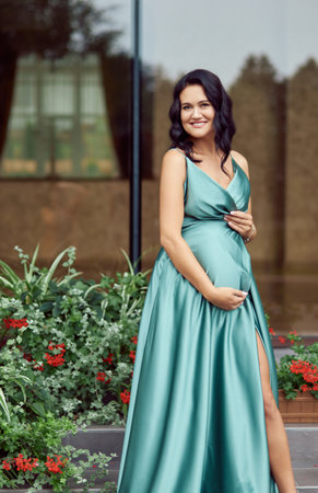 Luxurious pregnant lady. Outdoors portrait of a beautiful emotional young pregnant woman in a green dress.の写真素材