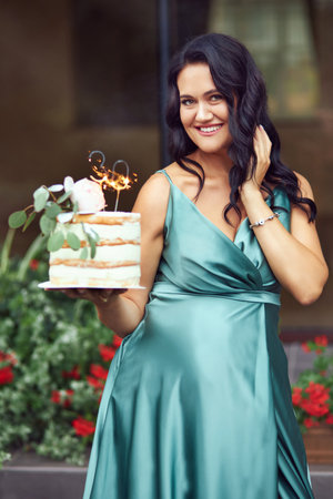 A happy pregnant brunette in a green dress is holding a birthday cake with a 30th birthday candle. pregnant woman expecting a baby and celebrating her birthday.の写真素材