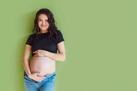 Pregnant woman smiles and hugs her belly on a green background, place for text.の写真素材