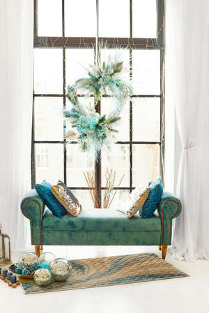 The window is large in a modern apartment. The blue sofa near the panoramic window is decorated with New Years decor.の写真素材