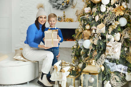 Caucasian mother and her little son spend time together near the Christmas tree, give gifts, make wishes together. family and winter holidays concept.の写真素材