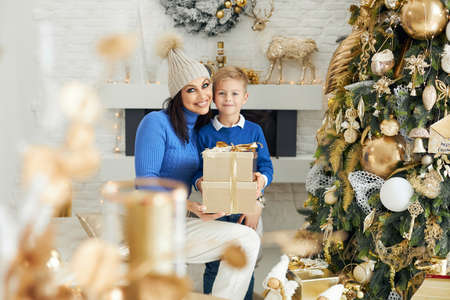Caucasian mother and her little son spend time together near the Christmas tree, give gifts, make wishes together. family and winter holidays concept.の写真素材