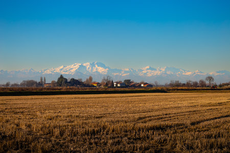 Snow-Covered Mountain Range Behind Rural Agricultural Fields and Village Housesの写真素材