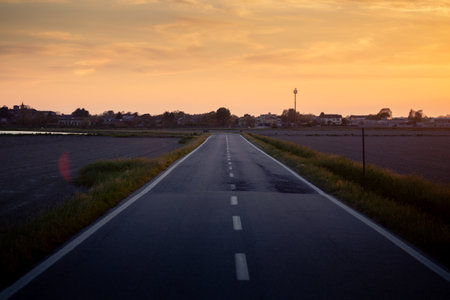 Empty Country Road at Sunset with Calm Orange Sky and Vast Fields
