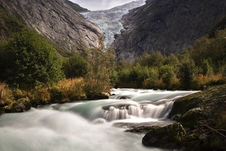 Landscape showing Briksdal glacier in a rocky valley with trees and a river in long exposure pictureの写真素材
