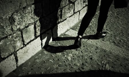 Woman legs walking in a medieval town street and its shadowの写真素材