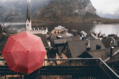 Girl holding a red umbrella looking at Hallstatt tourist town in Austria in a rainy dayの写真素材