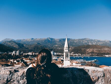 Girl looking at Budva beautiful coast town in Montenegro with a tower of a church standing out and...