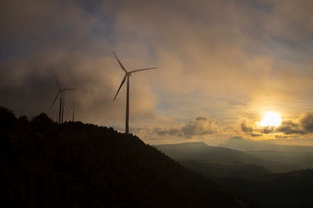 Sunset cloudy landscape showing some mountains and wind turbinesの写真素材