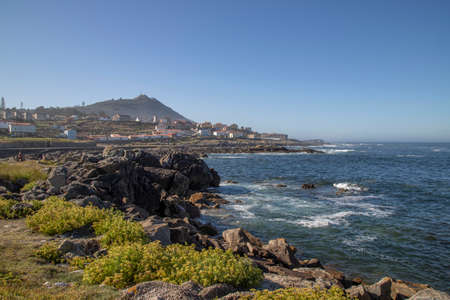 Seascape showing some rocks and plants and a town and a mountain in the foreground in A Guarda in Galicia Spainの写真素材