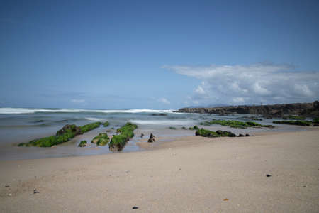 As Furnas beach long exposure picture showing extended rocks covered by green seaweeds under a blue...