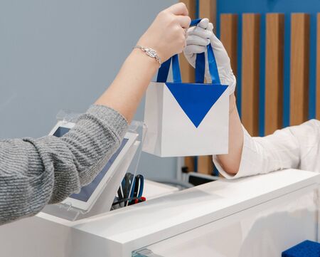 Seller passes after payment a white with blue package with a purchase to the buyer in the shopの写真素材